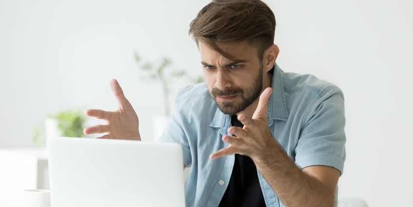 Man sitting in front of a computer appearing frustrated.