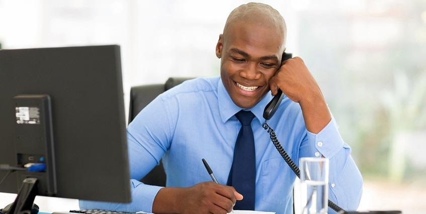 Man on the phone in front of a desktop computer.