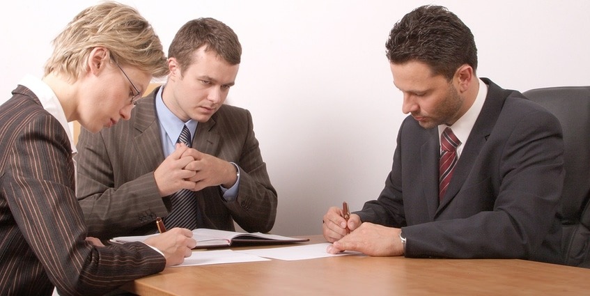 Three people in business suits meeting around a table