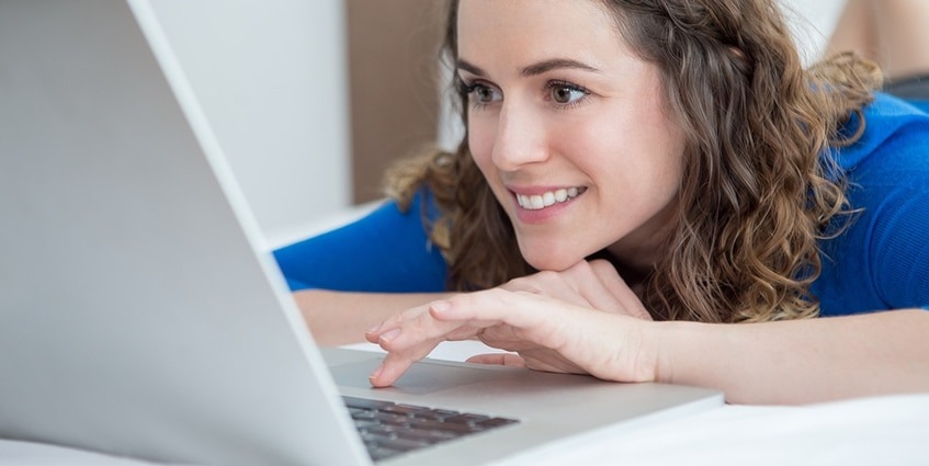 Woman lying on the floor looking at her laptop.